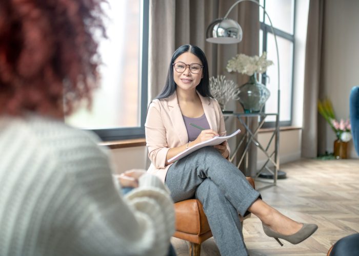 Pleasant psychologist. Pleasant psychologist wearing grey trousers smiling to client while speaking with her